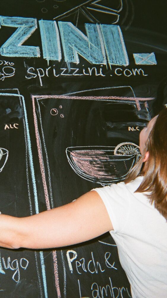 A guest reaching across the chalkboard menu under the Sprizzini lettering