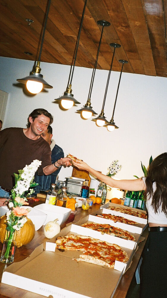 A slice of pizza being handed down a long table of open pizza boxes