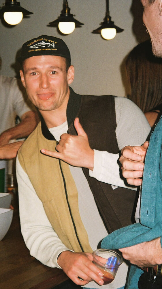 A guest in a cap throwing a shaka with a drink in his other hand