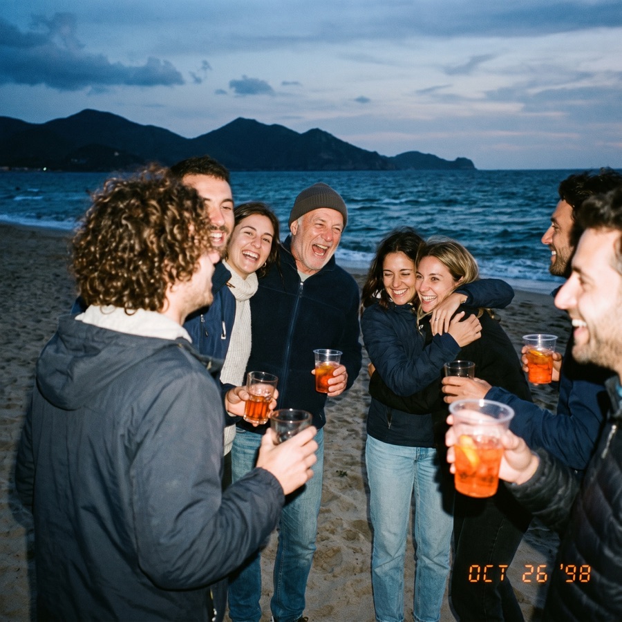 Friends together on the sand at dusk, everyone holding a Sprizzini