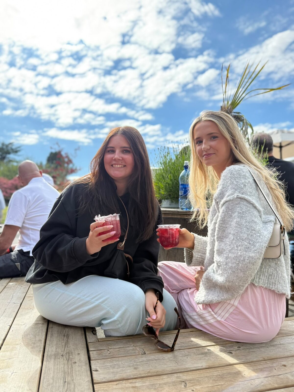 Two friends on a picnic bench with spritzes, water and mountains behind