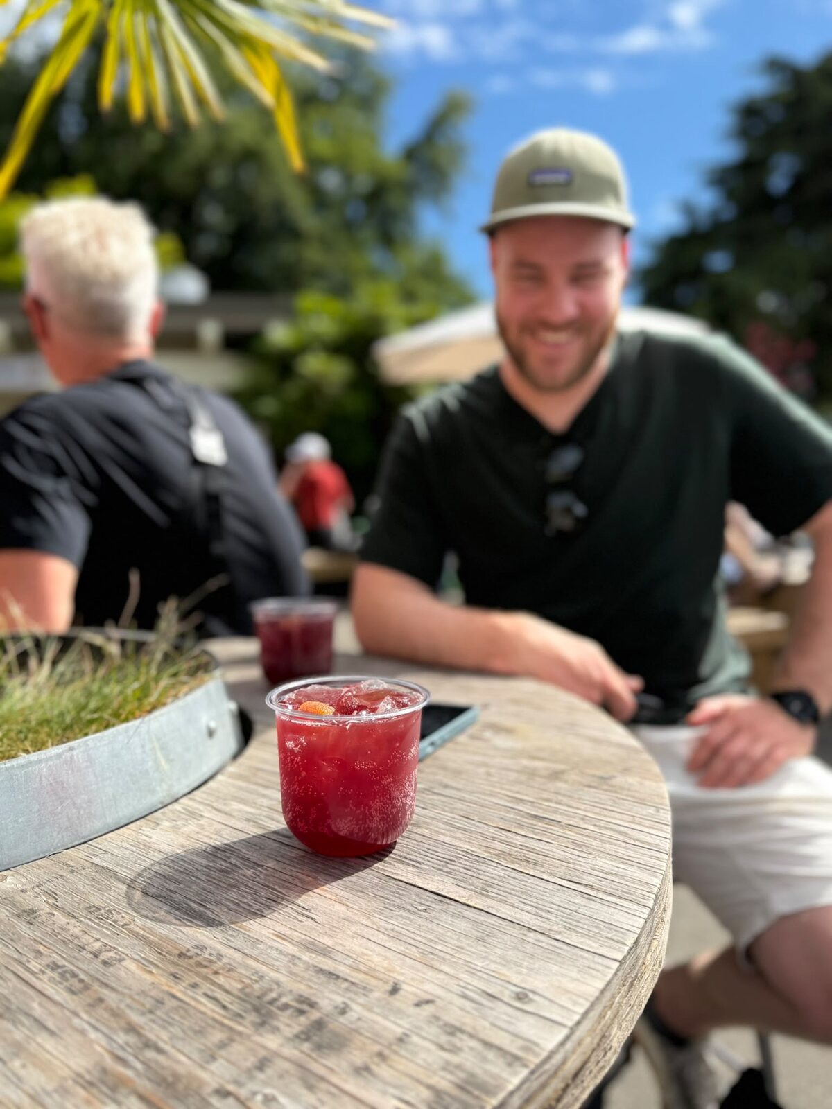 A spritz in focus on a round patio table, a man laughing behind it