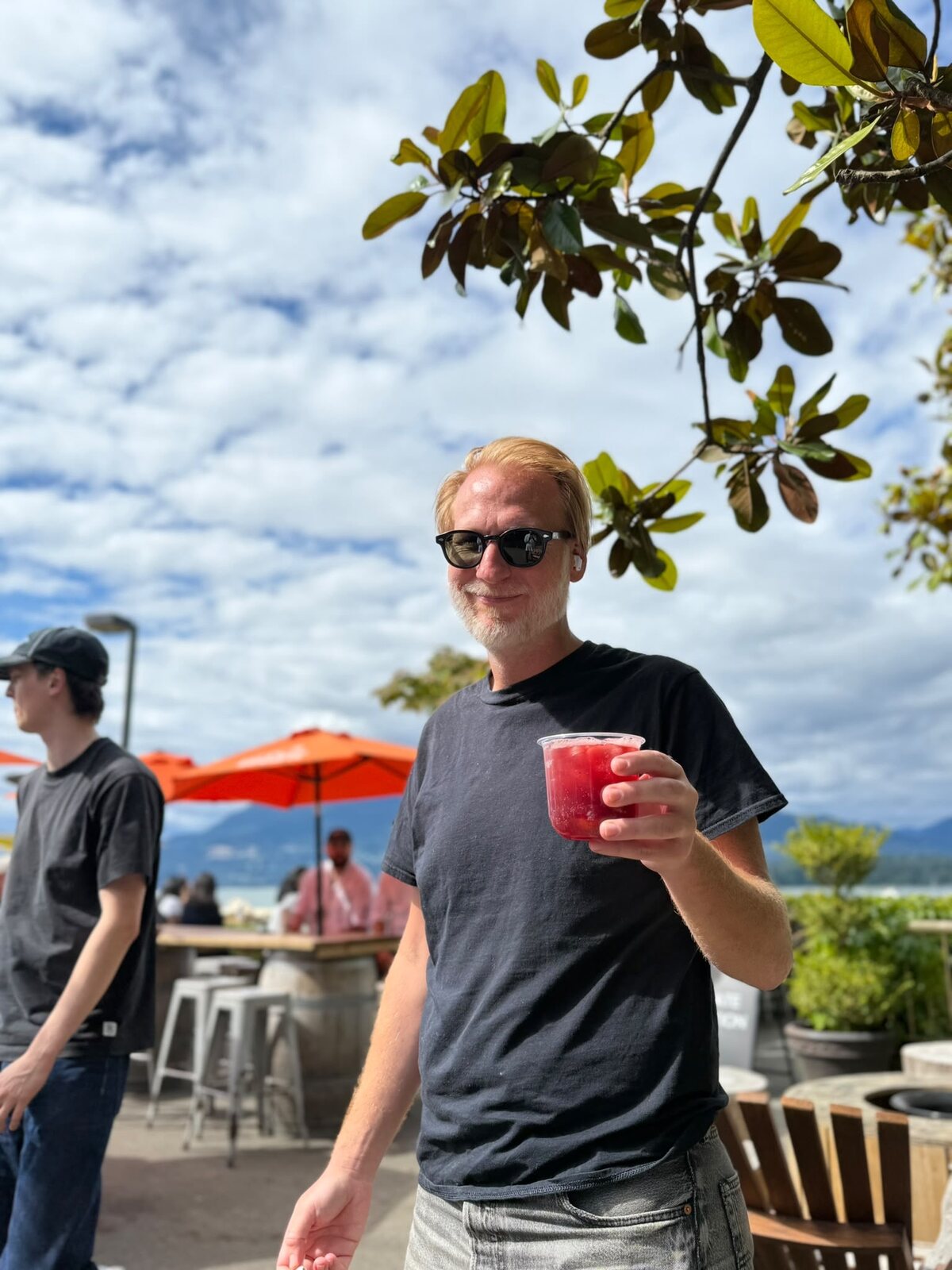 A man raising a Sprizzini on a sunny patio under a magnolia